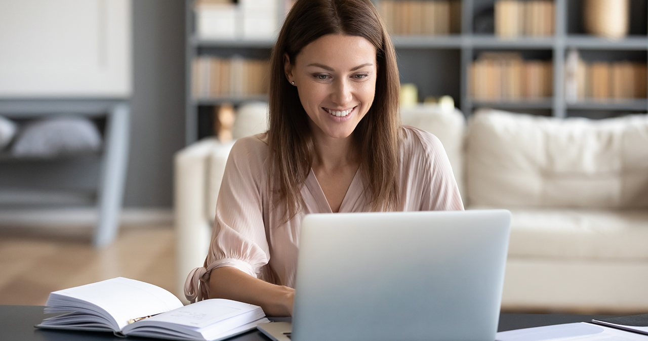 Head shot young happy woman sitting at desk, working from home on computer. Pleasant attractive smiling lady looking at laptop screen, shopping, chatting in social networks, studying online remotely.