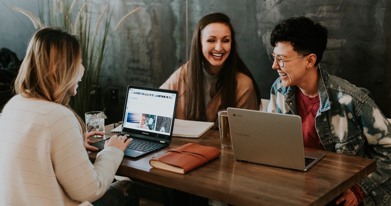 Three employees sat around a desk smiling and laughing