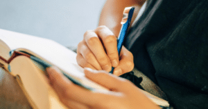 Individual writing in a note book with a ballpoint pen
