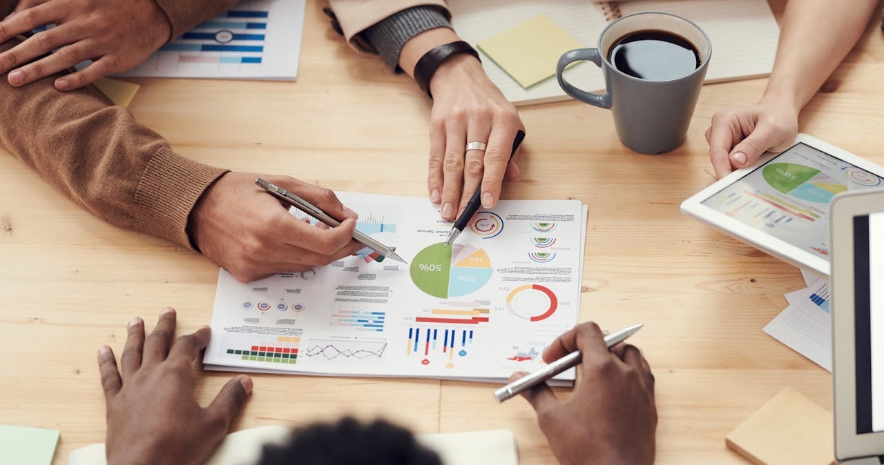 A visual report lies on a table, with hands of meeting participants visible around it