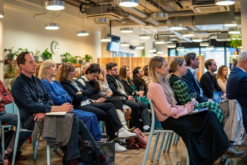 The side view of rows of an audience sitting down and facing a stage