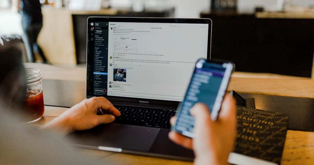 A man using his phone while sat at his desk with laptop
