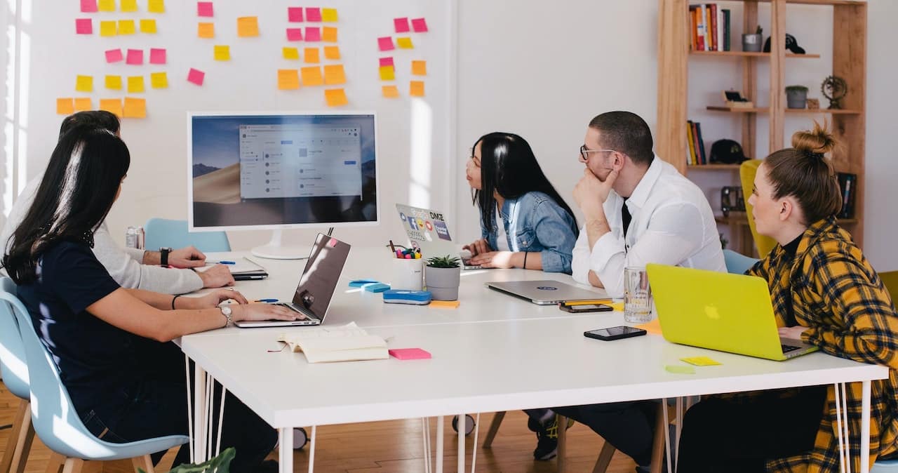 Four people sit around an office table looking at a screen and whiteboard in a strategy meeting