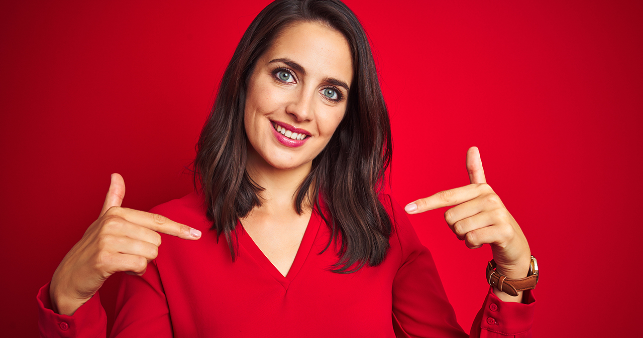 Young beautiful woman wearing shirt standing over red isolated background looking confident with smile on face, pointing oneself with fingers proud and happy.