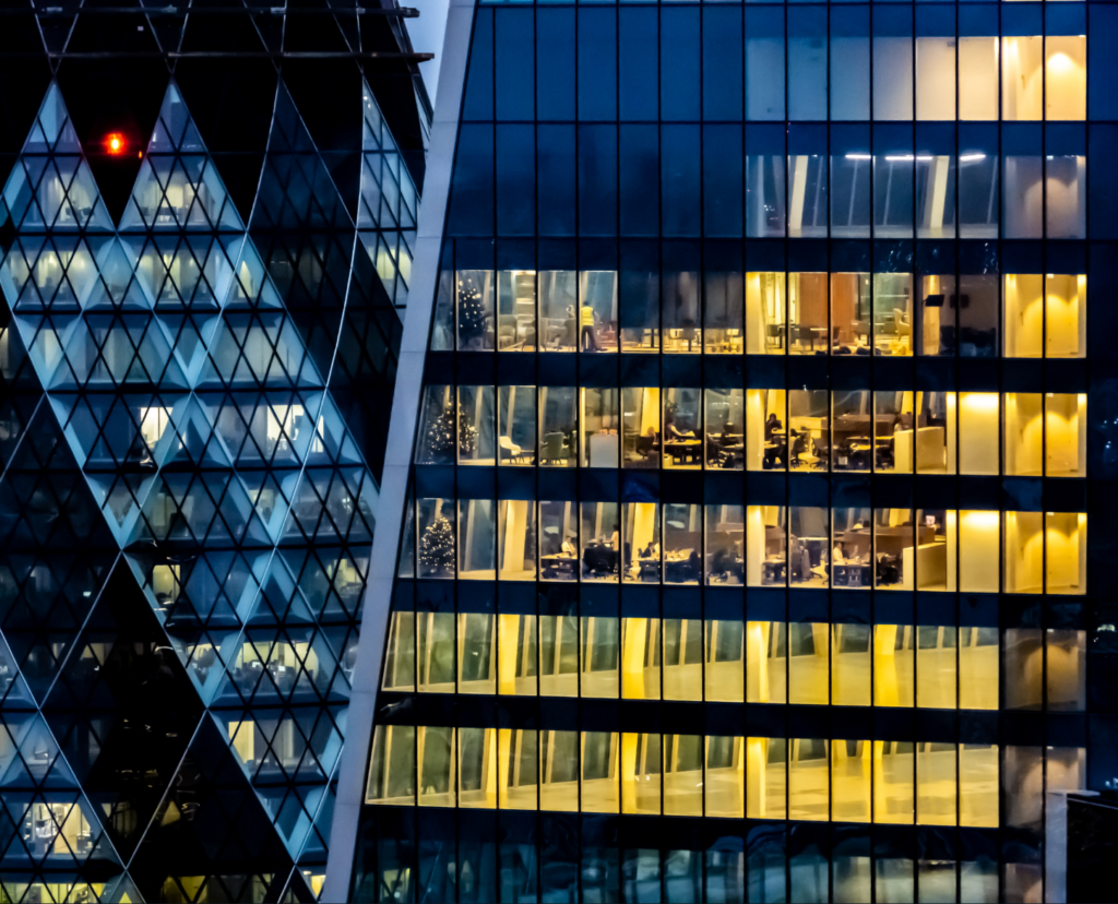 A glass skyscraper at night with yellow lights in many of the offices